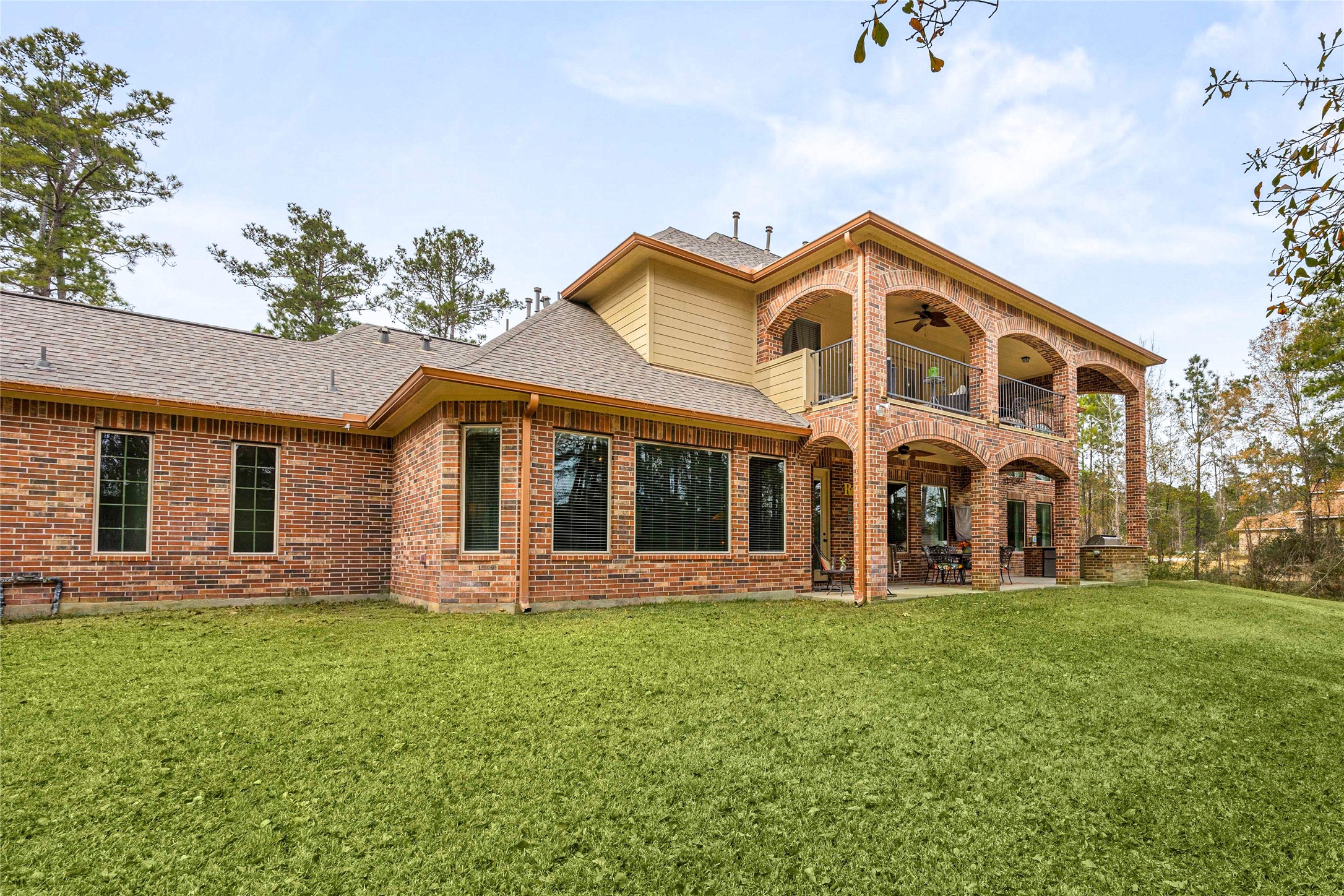 23421 Cannondale Loop Montgomery, TX 77316 - Photo 34 of 47 Impressive rear elevation showcasing classic brick architecture, expansive windows, and dual-level covered patios ideal for relaxing or entertaining. The spacious backyard offers plenty of room for gatherings, play, or future outdoor enhancements, all set against a backdrop of mature trees for added privacy and tranquility.