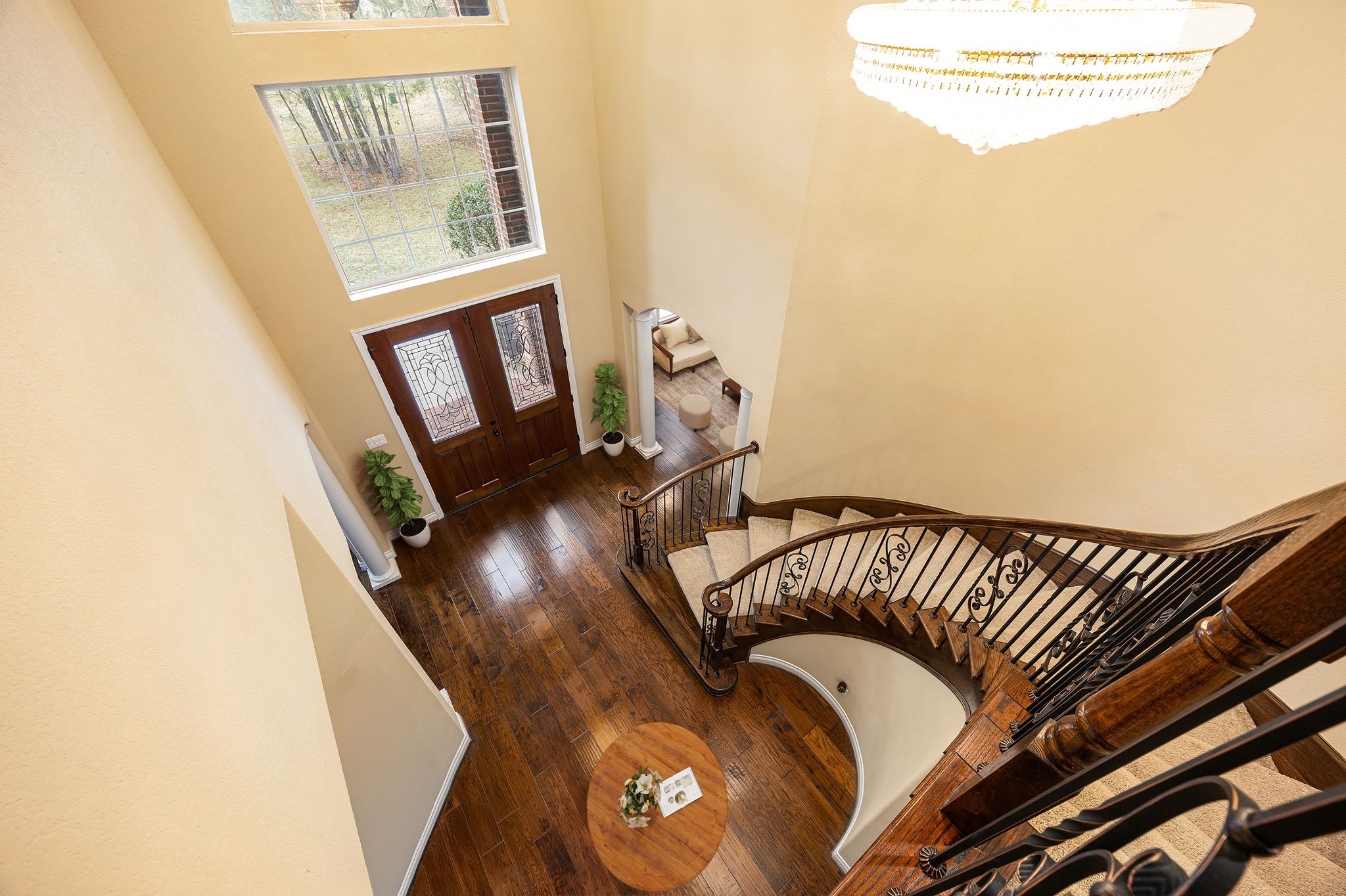 23421 Cannondale Loop Montgomery, TX 77316 - Photo 5 of 47 Grand entryway featuring soaring ceilings, rich hardwood floors, and a stunning curved staircase with wrought-iron railings. The space is filled with natural light from expansive windows, enhanced by a statement chandelier that adds warmth and sophistication, setting the tone for the elegance found throughout the home.