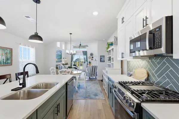 a kitchen with stainless steel appliances granite countertop a stove a sink dishwasher and white cabinets with wooden floor