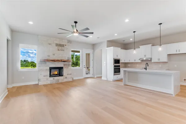 a view of an empty room and kitchen with fireplace ceiling fan