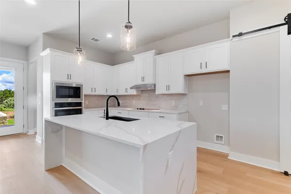 a kitchen that has a sink a microwave oven a stove and white cabinets with wooden floor