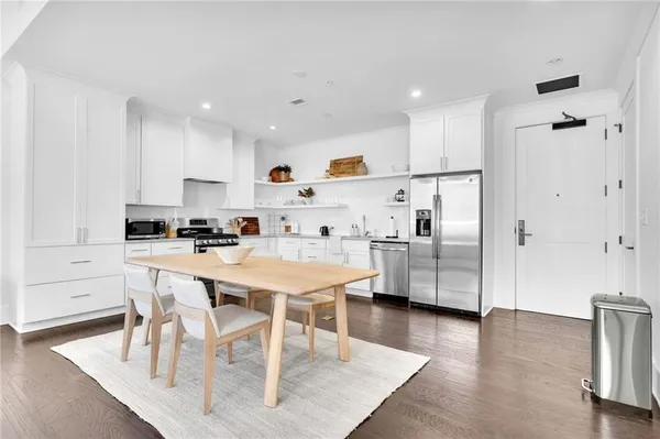 a kitchen with stainless steel appliances granite countertop a refrigerator a sink a stove a dining table and chairs with wooden floor