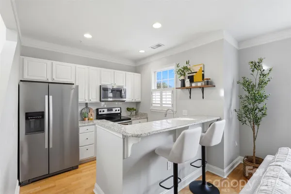 a kitchen with stainless steel appliances granite countertop a refrigerator a sink a stove a dining table and chairs with wooden floor