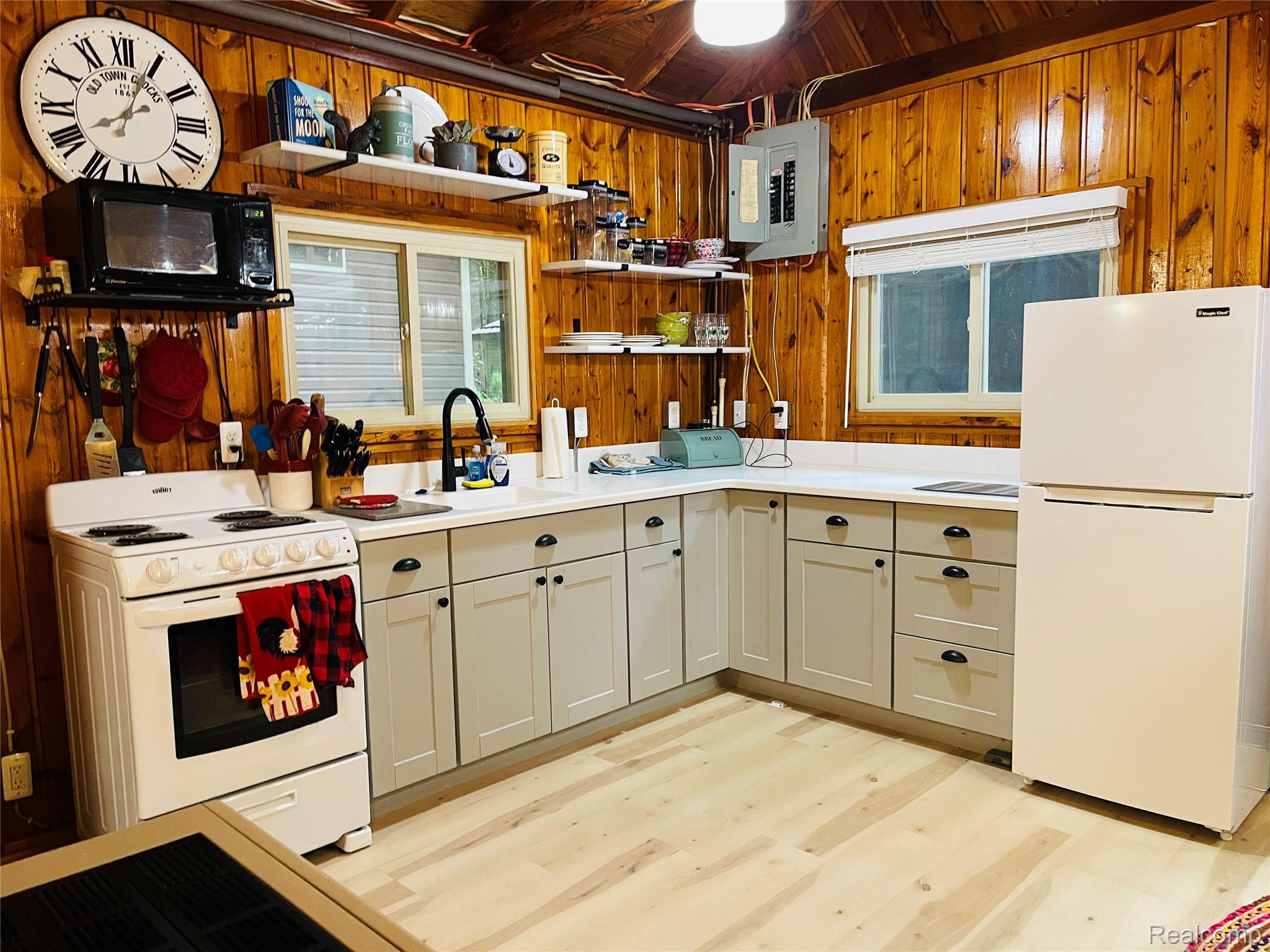 417 Ogemaw Road Rose City, MI 48654 - Photo 3 of 26 Corner kitchen with light wood-finish flooring, light grey cabinetry with dark hardware, white countertops, and wood paneling