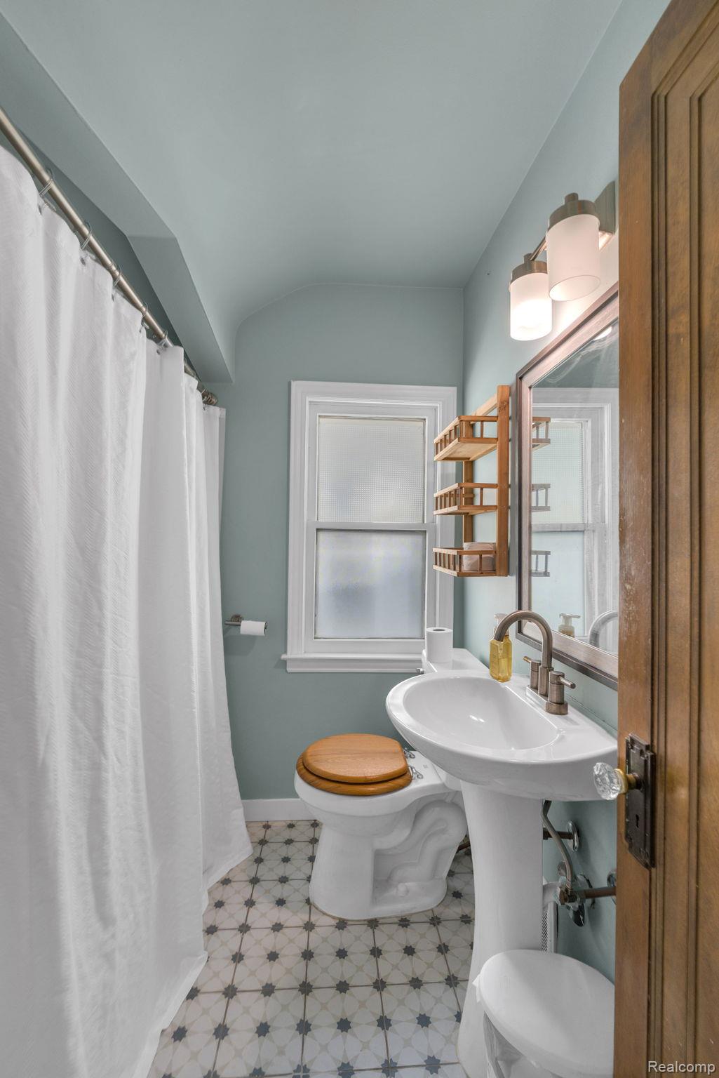7631 Maple Street Dearborn, MI 48126 - Photo 35 of 48 Pedestal sink, patterned floor tiling, window, wall-mounted light fixture, and wood-panel door