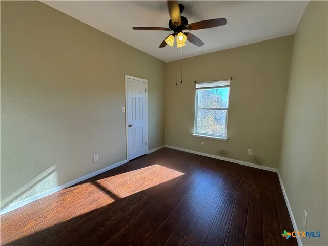 an empty room with wooden floor chandelier fan and windows