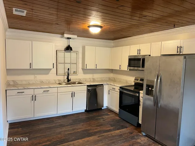 a kitchen with stainless steel appliances granite countertop a refrigerator a sink dishwasher a stove and white countertops with wooden floor