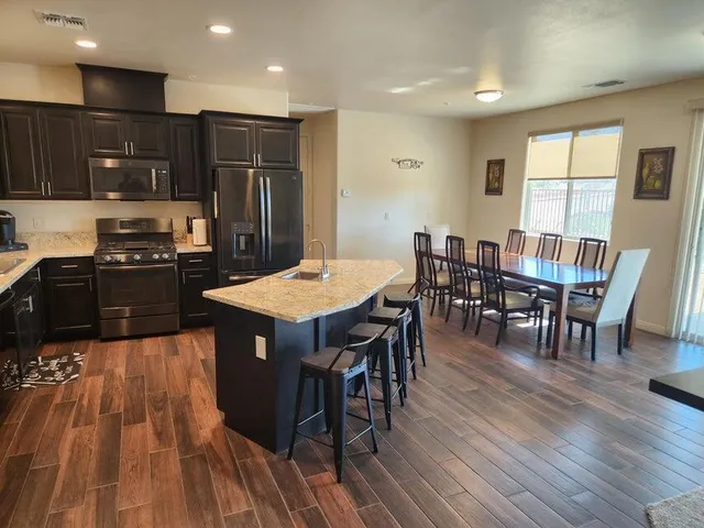 a kitchen with stainless steel appliances granite countertop a stove a refrigerator a kitchen island a dining table and chairs with wooden floor