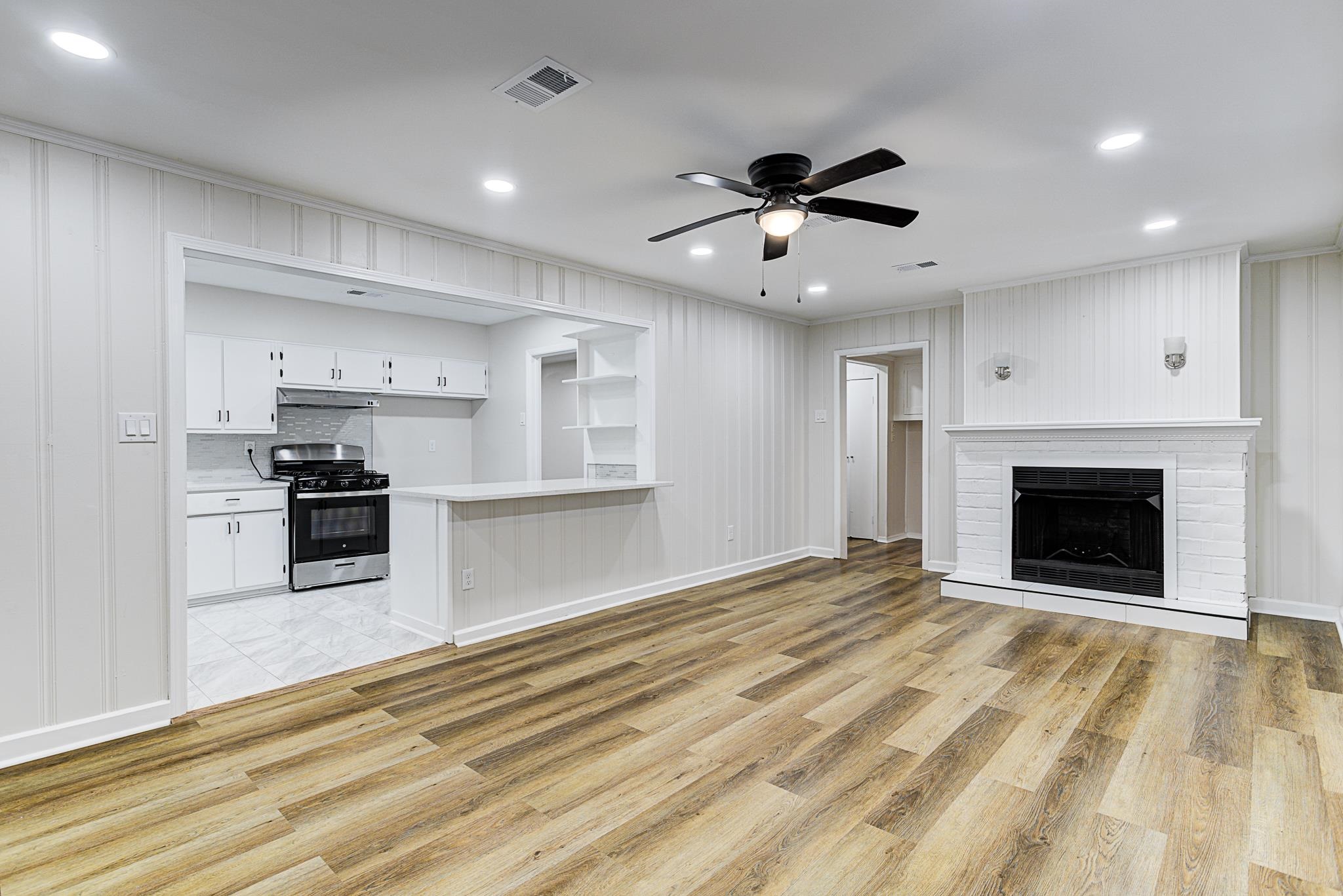 5094 Lochinvar Road Memphis, TN 38116 - Photo 9 of 23 Kitchen, white cabinetry, laminate flooring, a brick fireplace, and stainless steel range with gas stovetop