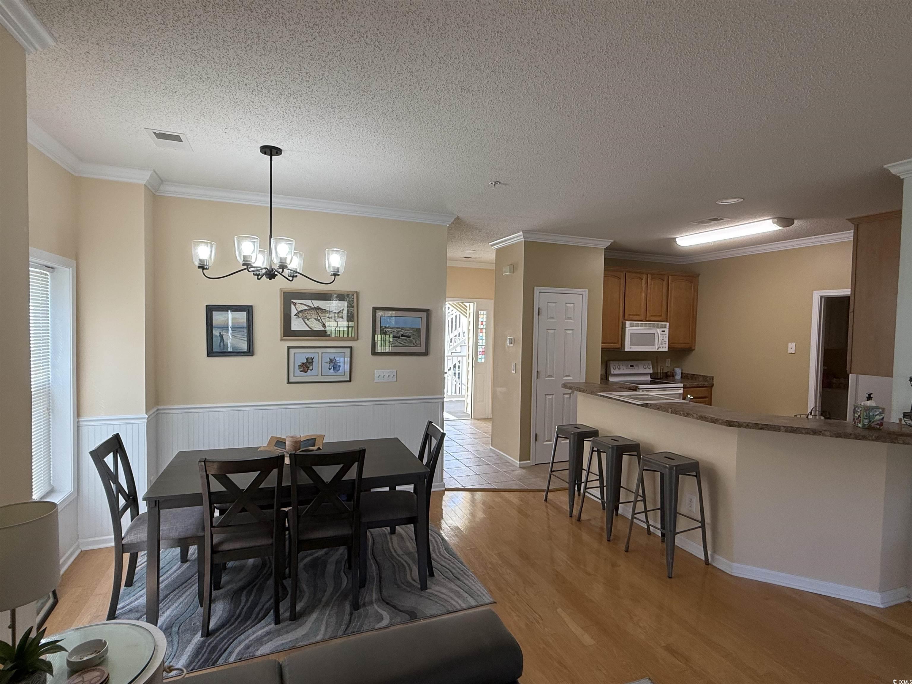 5858 Longwood Drive, Unit #204 Murrells Inlet, SC 29576 - Photo 8 of 13 Dining space with ornamental molding, a textured ceiling, a chandelier, light wood finished floors, and a wainscoted wall