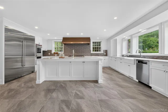 a large white kitchen with a sink large window and stainless steel appliances