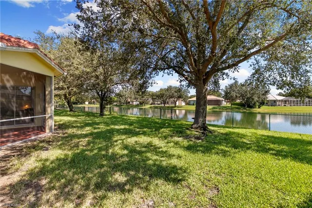 a view of a white house in front of a yard with plants and large trees