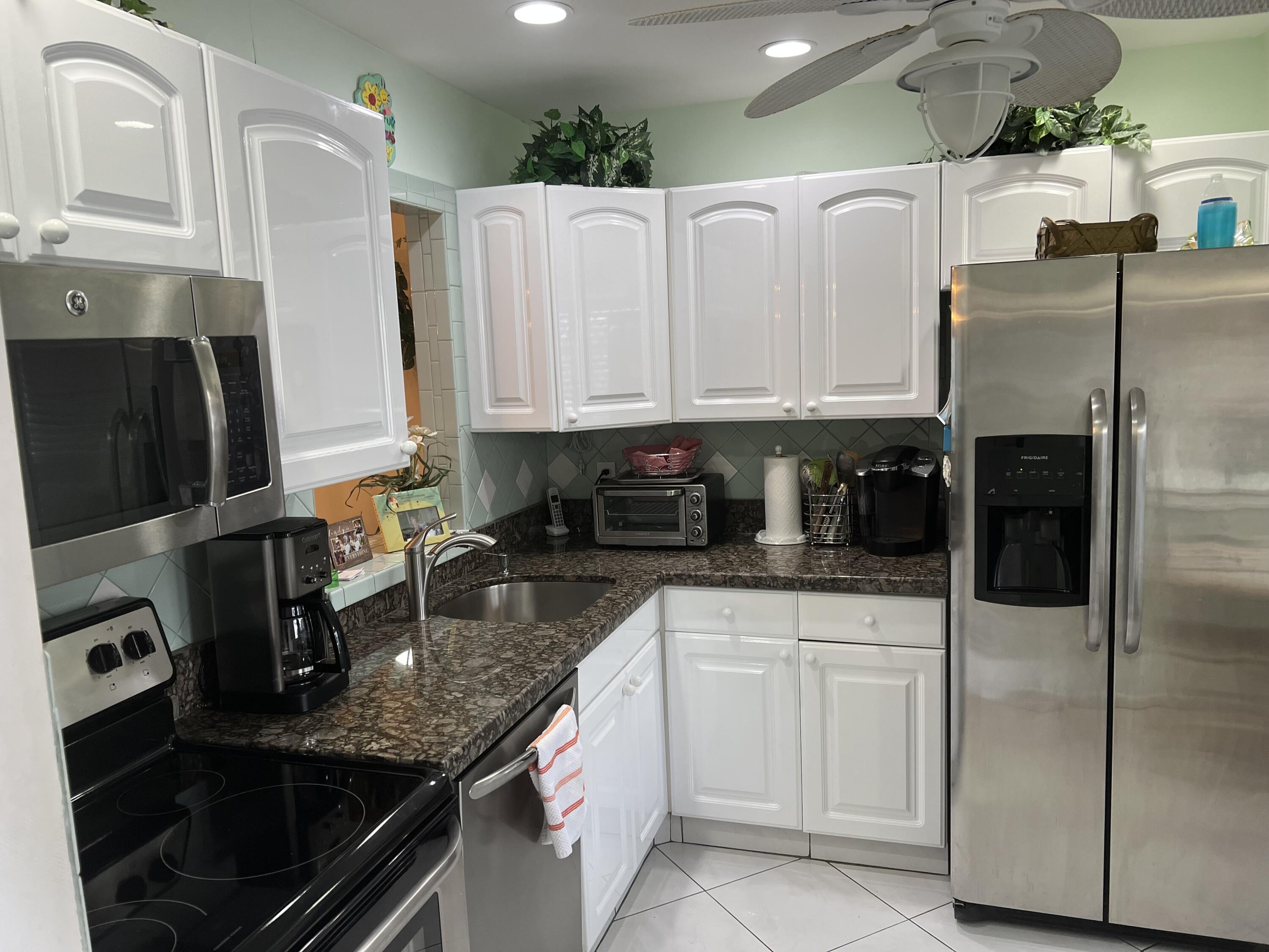 6877 Moonlit Drive Delray Beach, FL 33446 - Photo 18 of 45 a kitchen with granite countertop a refrigerator a sink and white cabinets