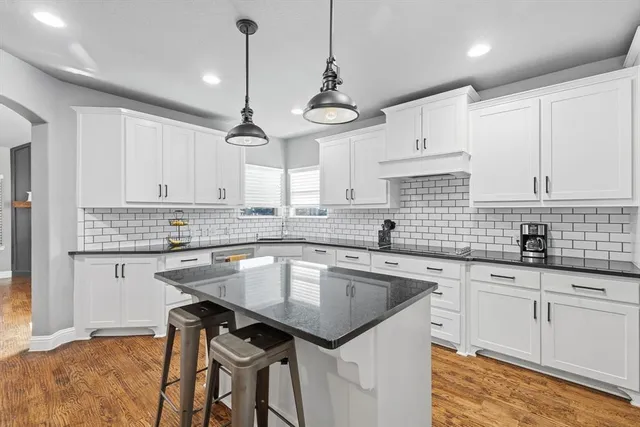 a kitchen with stainless steel appliances granite countertop a sink dishwasher and white cabinets with wooden floor