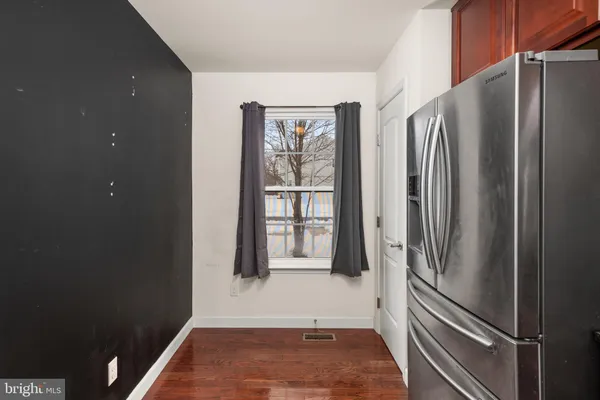 a view of a refrigerator in kitchen and an empty room with wooden floor