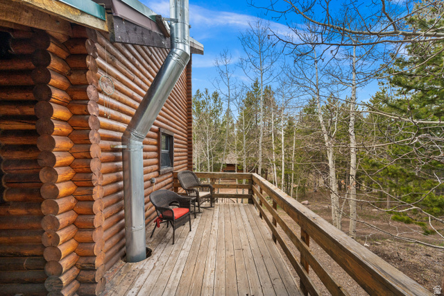 4725 Pine Ridge Road Evanston, UT 82930 - Photo 38 of 82 Expansive wood deck with a natural wood railing, featuring a log cabin exterior and mature trees beyond