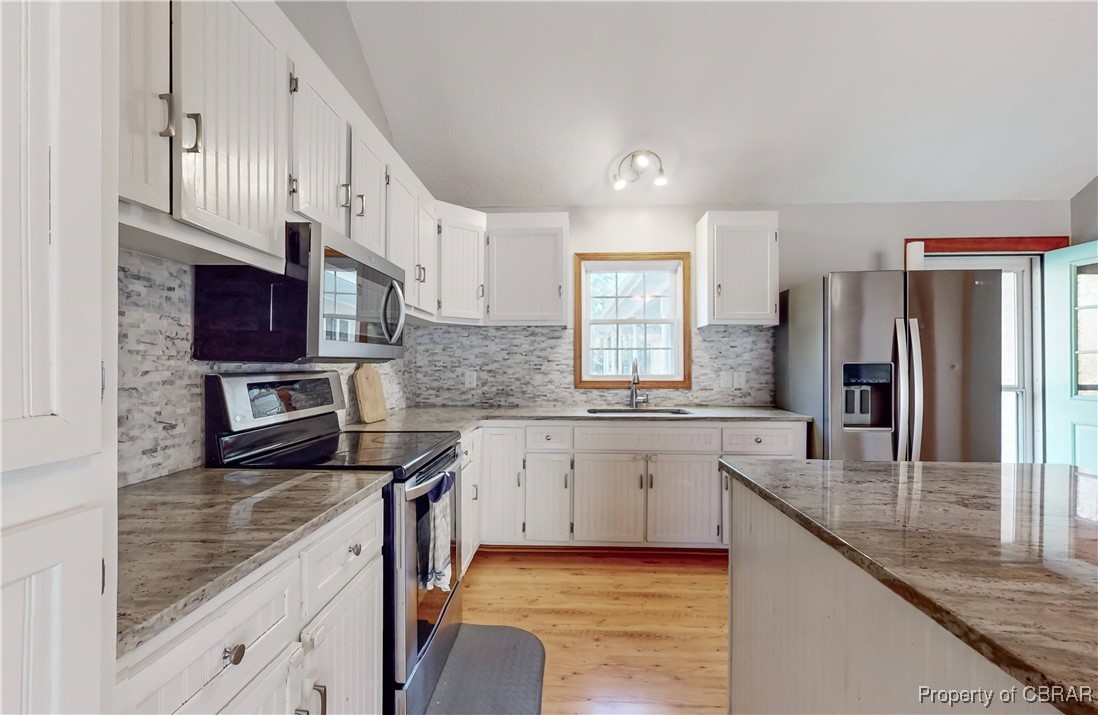 Kitchen with backsplash, light hardwood / wood-style floors, stone countertops, stainless steel appliances, and white cabinets
