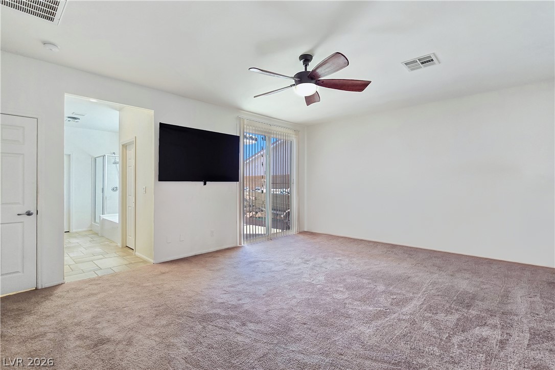 2485 Morrow Ridge Place Laughlin, NV 89029 - Photo 22 of 40 A spacious primary bedroom features soft carpeting, a ceiling fan, and direct access to a private bathroom and outdoor area.