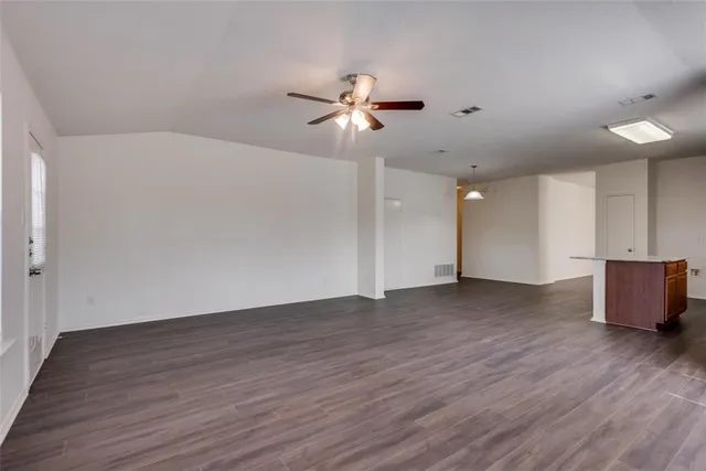 a view of an empty room with wooden floor and a ceiling fan