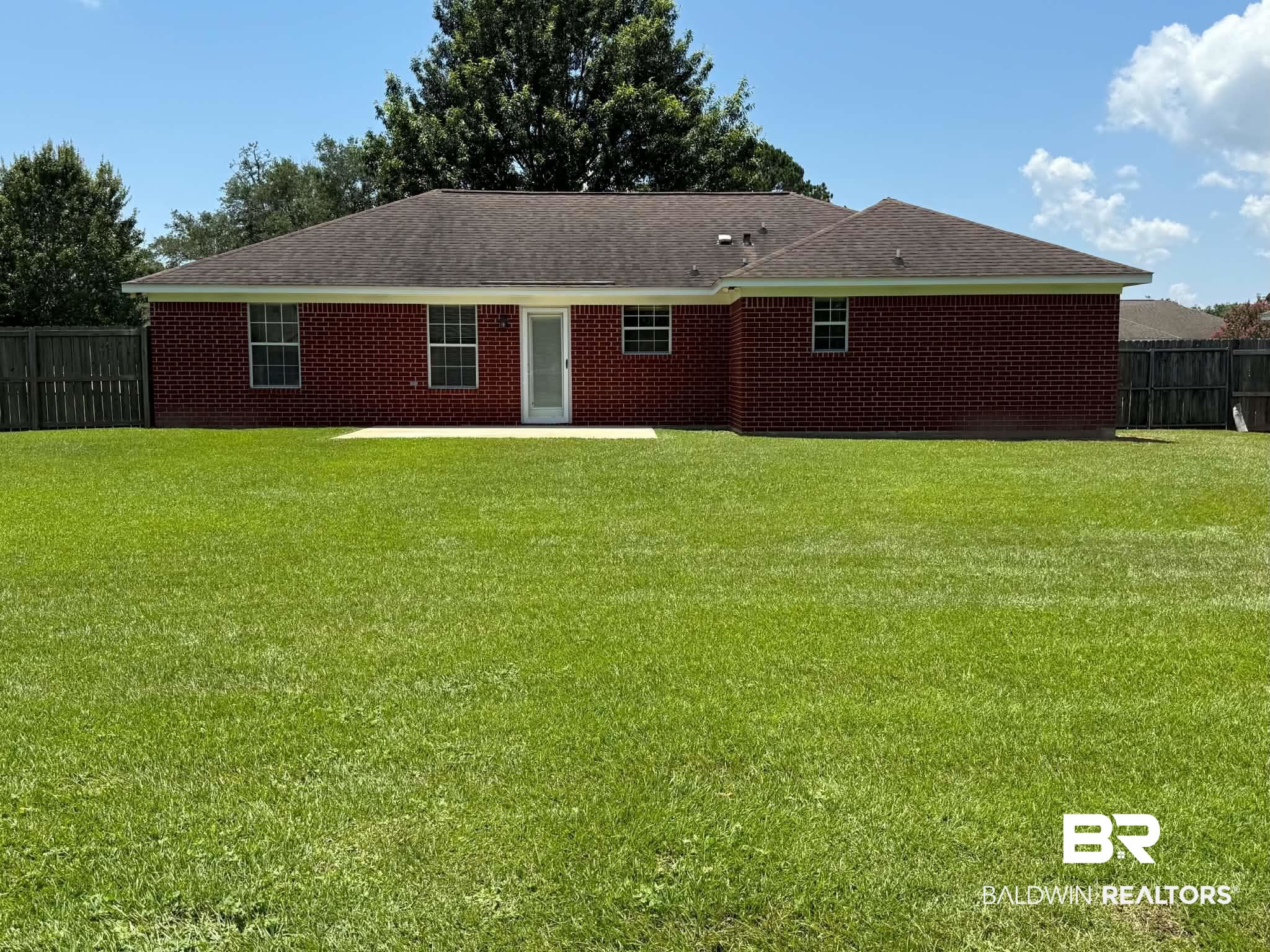 123 Pennbrooke Loop Foley, AL 36535 - Photo 7 of 49 Expansive green lawn with a red brick exterior, a white back door, and multiple windows, all framed by a wood privacy fence