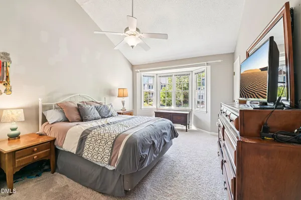 a spacious bedroom with a bed and a flat tv screen on dresser