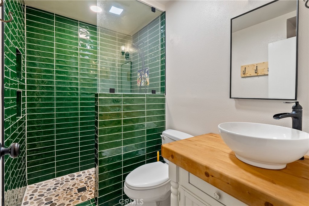 8892 Palomar Avenue Atascadero, CA 93422 - Photo 22 of 49 Stunning bathroom featuring a green subway tile shower with glass doors, a natural rock shower floor, and a vessel sink accented with sleek black fixtures.