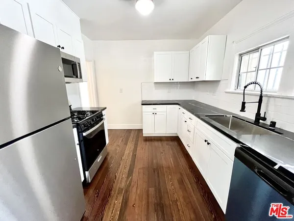a kitchen with granite countertop a refrigerator a sink a stove and white cabinets with wooden floor