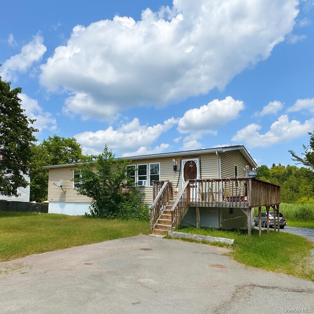 Manufactured / mobile home with a wooden deck, a front lawn, and stairs