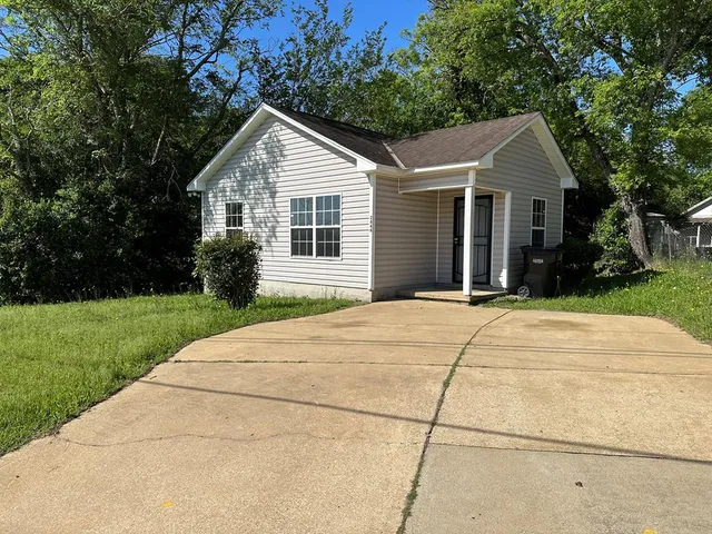 a view of a white house with a yard plants and large tree