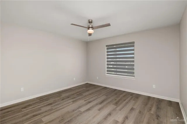 an empty room with wooden floor ceiling fan and window