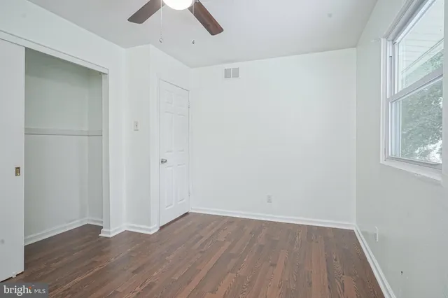 an empty room with wooden floor chandelier fan and windows