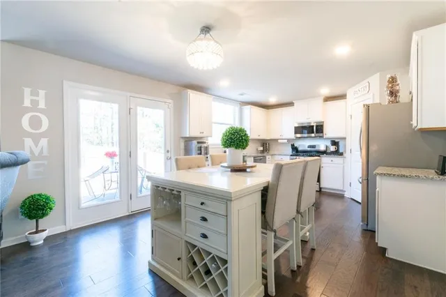 a kitchen with stainless steel appliances kitchen island granite countertop a refrigerator a sink dishwasher a stove a dining table and chairs with wooden floor