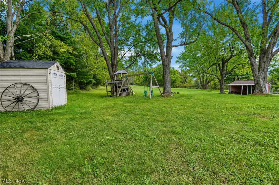 3864 State Road South Ashtabula, OH 44004 - Photo 40 of 50 Expansive grounds featuring mature shade trees and lush lawn, complemented by storage structures and rustic garden elements including a wagon wheel accent and swing set frame