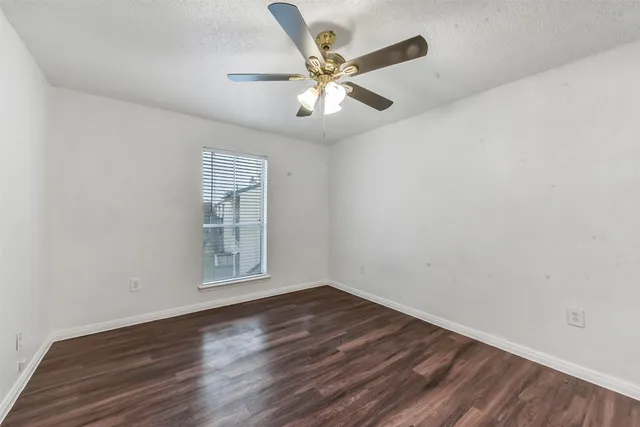 an empty room with wooden floor ceiling fan and windows
