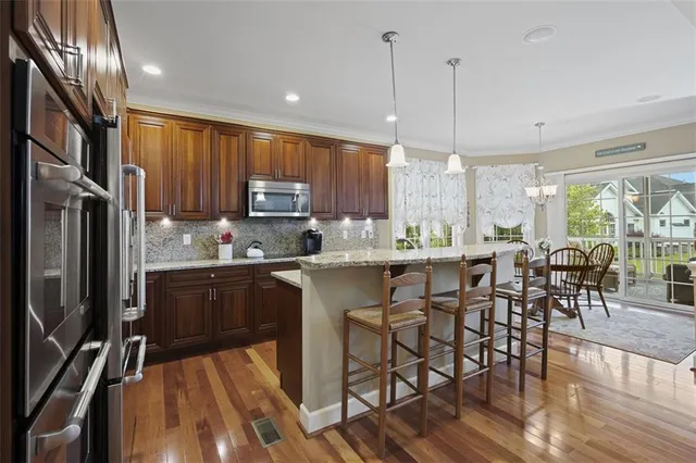 a kitchen with stainless steel appliances granite countertop a refrigerator a stove a sink a dining table and chairs with wooden floor