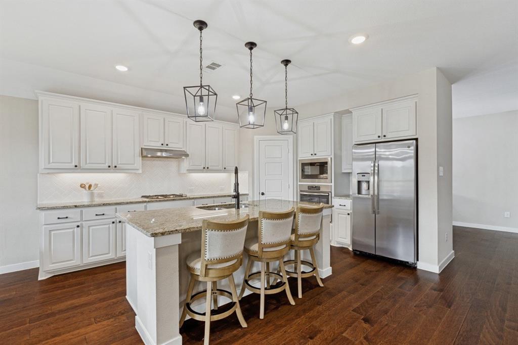4136 Lightstone Lane Celina, TX 75009 - Photo 12 of 39 a kitchen with stainless steel appliances kitchen island granite countertop a wooden floor and white cabinets