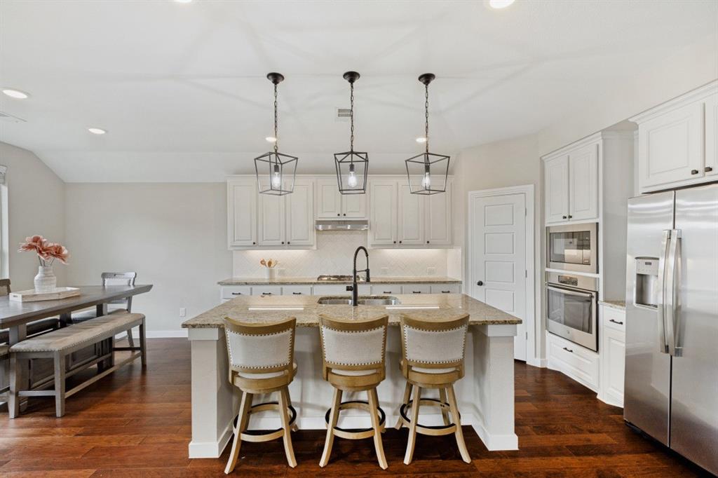 4136 Lightstone Lane Celina, TX 75009 - Photo 17 of 39 a kitchen with stainless steel appliances kitchen island granite countertop a dining table chairs and white cabinets