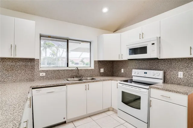 a kitchen with granite countertop white cabinets white stainless steel appliances a sink and a window