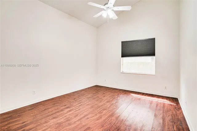 a view of an empty room with wooden floor and a ceiling fan