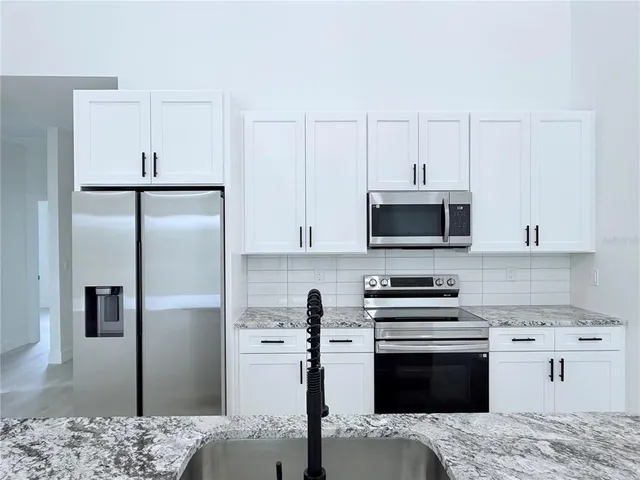 a kitchen with stainless steel appliances kitchen island granite countertop a refrigerator stove and white cabinets