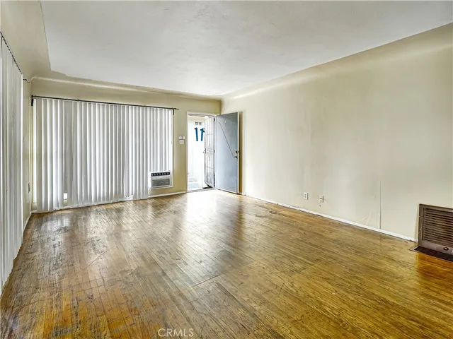 an empty room with wooden floor and windows with curtains