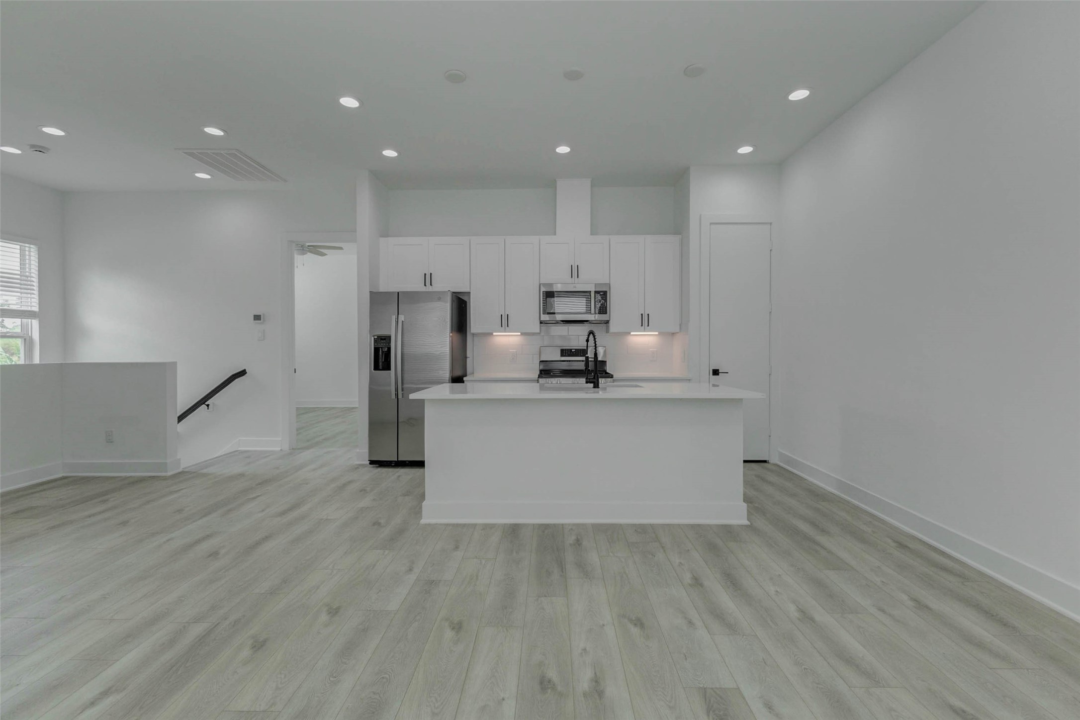 5705 Elysium Street Houston, TX 77091 - Photo 13 of 22 Modern kitchen and living area centered around a sleek white island with quartz-style counters, stainless appliances, black faucet, white cabinetry, and under-cabinet lighting. The open plan feels bright and refined, offering a stylish hub for cooking, casual dining, entertaining, and everyday connection.