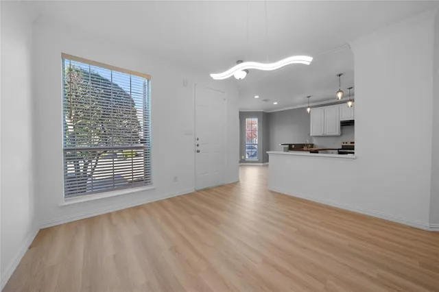 a view of an empty room with wooden floor and a kitchen