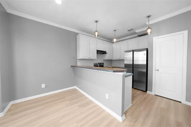 a kitchen with stainless steel appliances granite countertop a refrigerator a sink dishwasher a stove and white cabinets with wooden floor