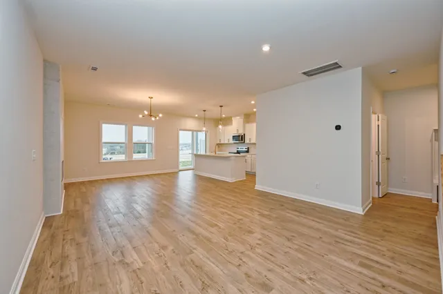 a view of an empty room and kitchen with wooden floor