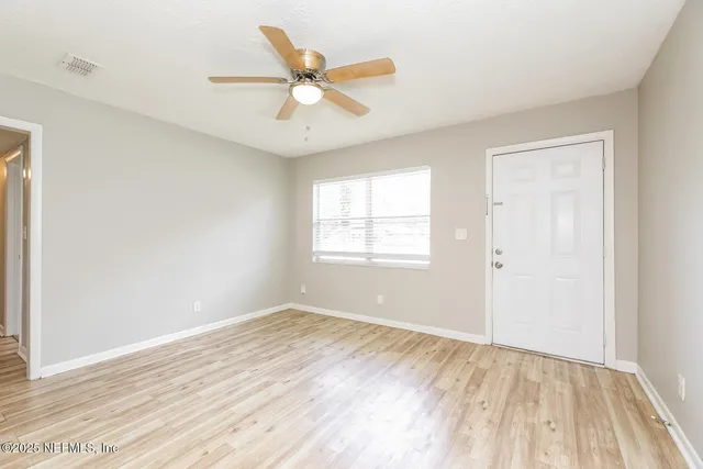 an empty room with wooden floor fan and windows