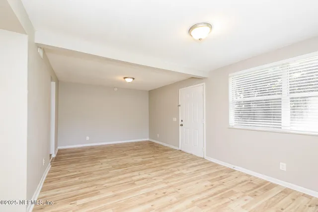a view of an empty room with wooden floor and a window