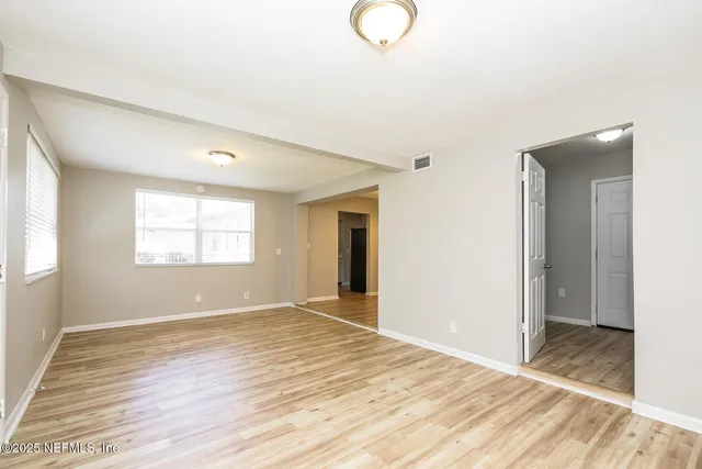 a view of an empty room with wooden floor and a window