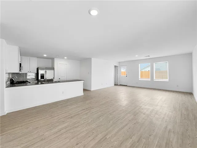 a kitchen with stainless steel appliances granite countertop a stove a sink dishwasher a refrigerator and white cabinets with wooden floor