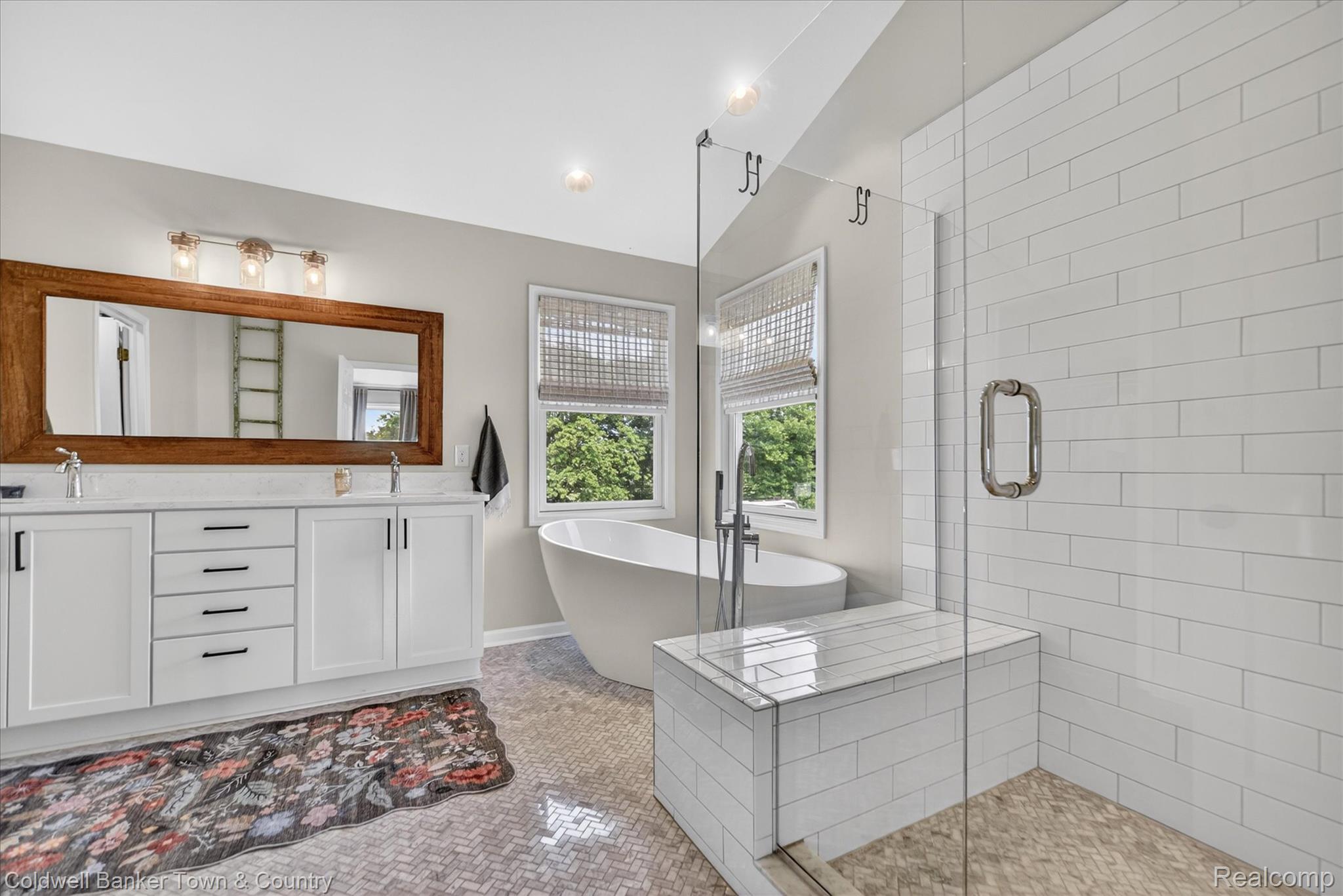 918 Gray Fox Court Howell, MI 48843 - Photo 32 of 84 Contemporary bathroom featuring a freestanding soaking tub, a spacious glass-enclosed shower with bench seating, and a dual-sink vanity with white cabinetry and a large wood-framed mirror